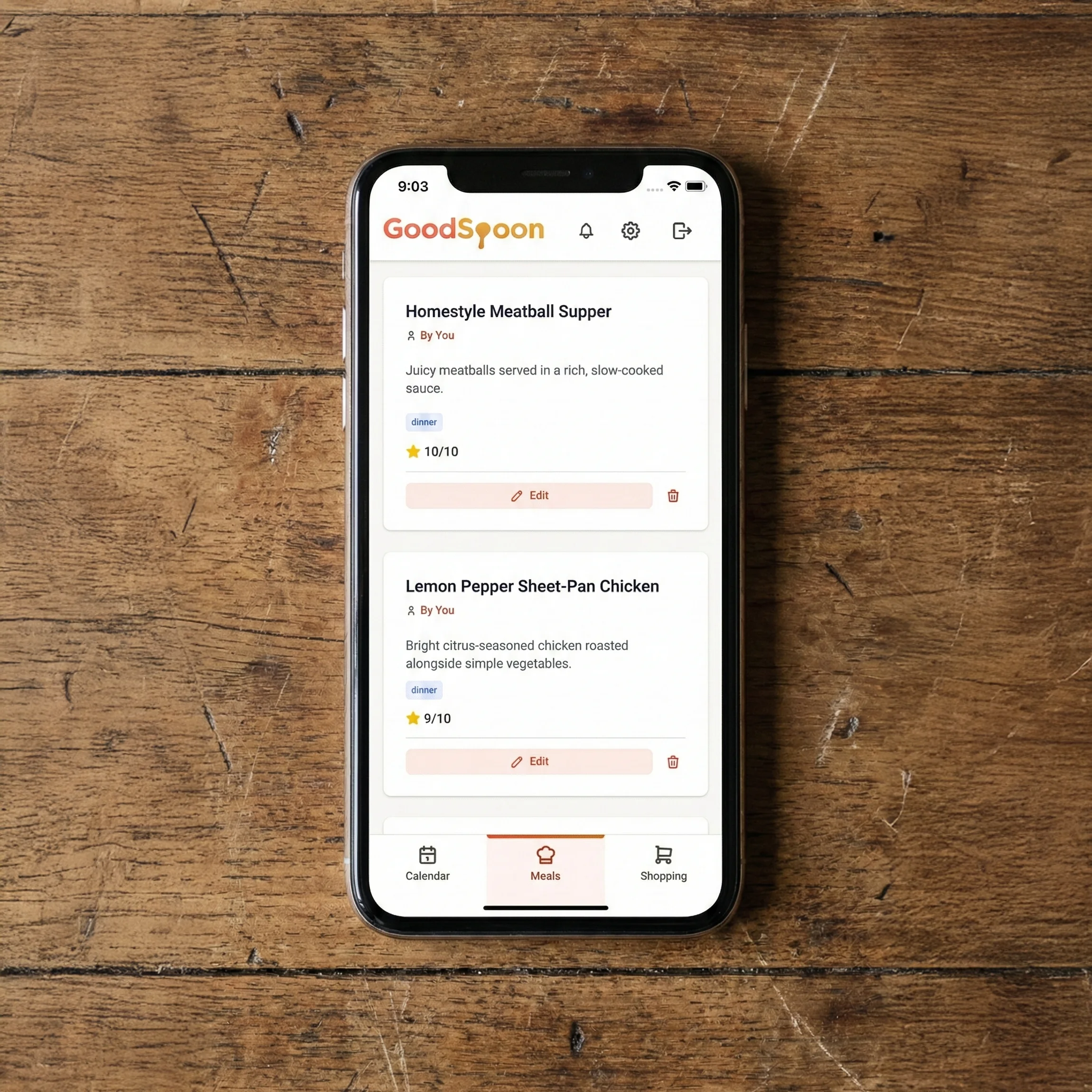 Smartphone displaying GoodSpoon meals page on wooden table, showing organized digital cookbook with recipe categories and favorites